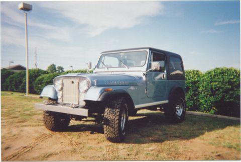 1984 Jeep Wrangler - A blue Jeep CJ-7 is parked on a grassy area under a bright blue sky.