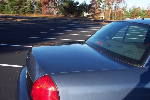2001 Ford Crown Victoria - The rear of a dark blue sedan is shown in a parking lot with trees in the background.