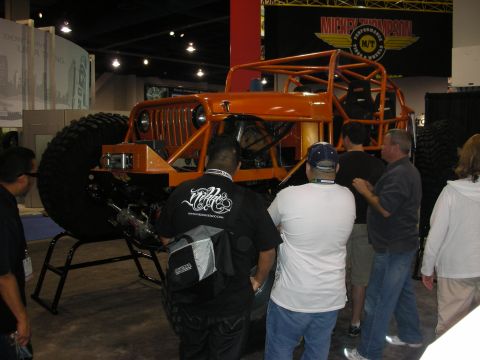 1998 Ford Crown Victoria - An orange custom off-road vehicle is displayed indoors with several people observing it.