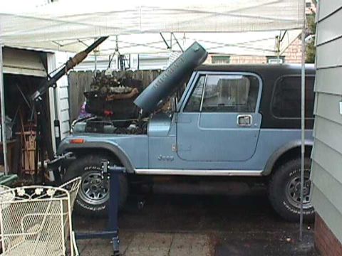1984 Jeep Wrangler - A blue 1984 Jeep Wrangler is parked outside with its engine removed and hoisted by a crane.