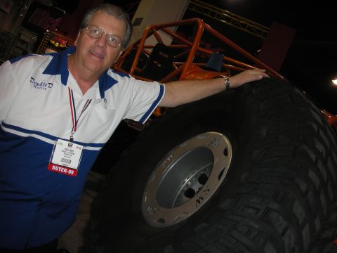 1998 Ford Crown Victoria - Man poses with a very large tire, likely from a custom off-road vehicle at an event.