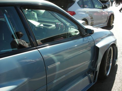1998 Ford Crown Victoria - A light blue car with a custom body kit is parked next to a white hatchback.