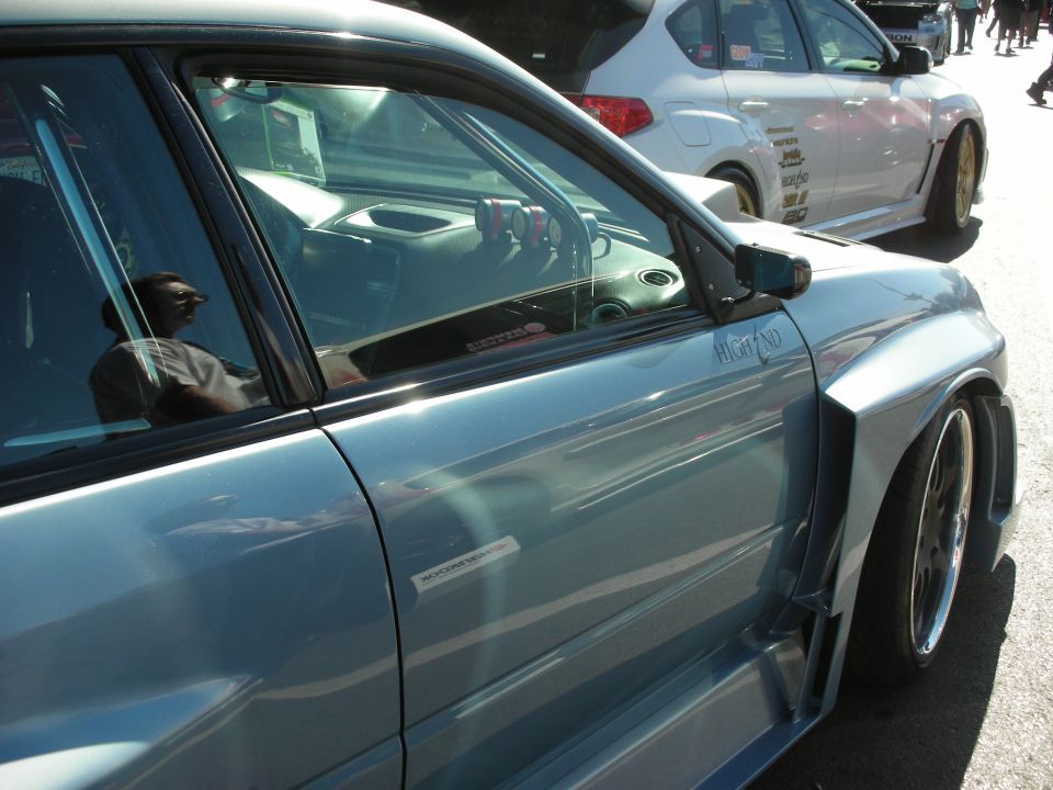 Light blue car with widebody kit, lowered suspension, and aftermarket gauges visible through the window