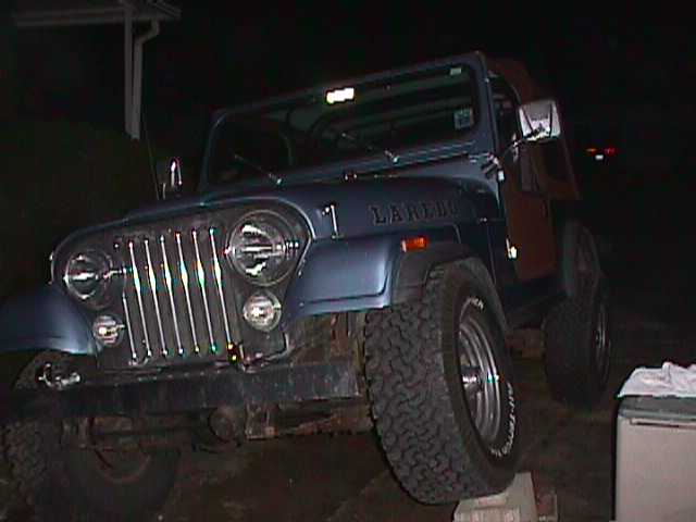 Blue Jeep CJ-7 Laredo with aftermarket wheels and tires, parked at night
