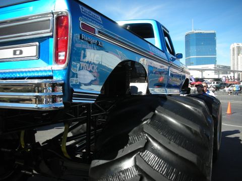 1998 Ford Crown Victoria - A blue monster truck is parked outdoors with a city skyline in the background.