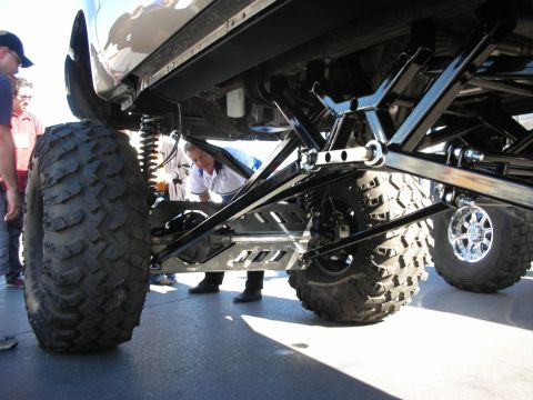 1998 Ford Crown Victoria - A custom truck's undercarriage is examined by onlookers, revealing its extreme modifications and large tires.