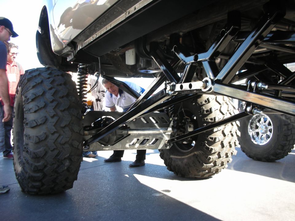 Underside view of a heavily modified truck with massive off-road tires and custom suspension components