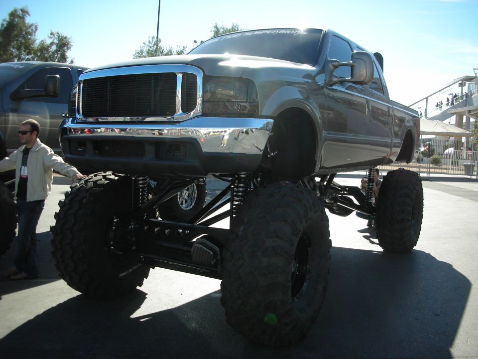Lifted pickup truck with huge tires and custom suspension. Another truck is parked behind it