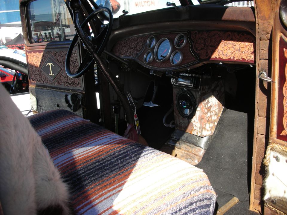 Interior of a vintage truck with custom leather tooling on the dash and doors. Features a striped seat cover and aftermarket gauges