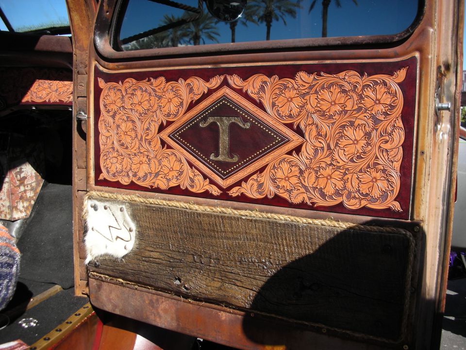 Interior door panel with ornate tooled leather and a wooden lower section, a diamond with the letter T