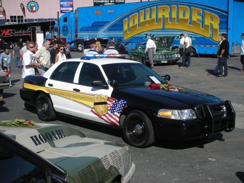 1998 Ford Crown Victoria - A 1998 Ford Crown Victoria police car is displayed with flowers on the hood and an American flag decal on the side.