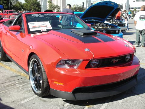 1998 Ford Crown Victoria - Red Ford Mustang convertible with racing stripes and custom hood pins is displayed outdoors.
