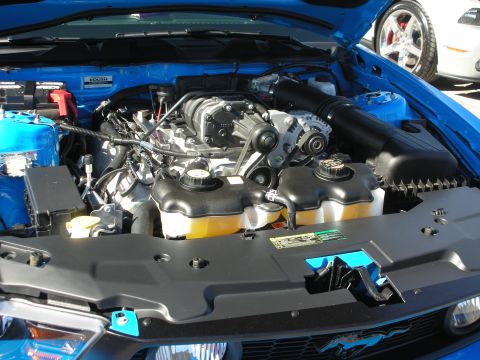1998 Ford Crown Victoria - Engine bay of a blue Ford Mustang, showing a supercharged V8 engine and another Mustang in the background.