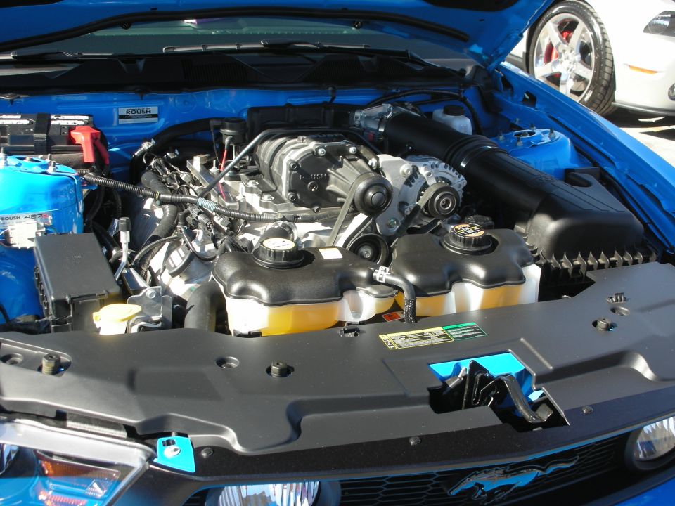 Blue Ford Mustang engine bay with supercharger; another Mustang visible in background