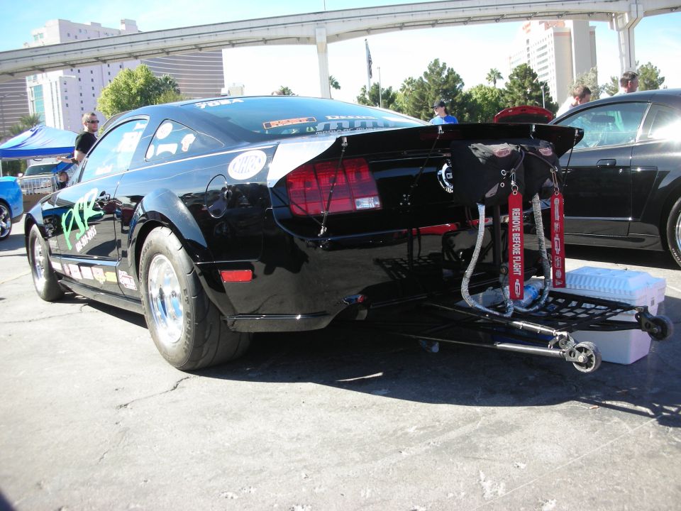 Black Ford Mustang drag car with large rear spoiler and drag chute, rear view