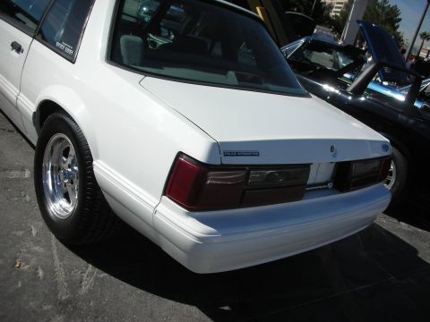 1998 Ford Crown Victoria - Rear view of a white police interceptor sedan with chrome wheels, parked beside another vehicle.