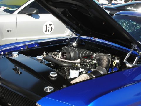1998 Ford Crown Victoria - Engine bay of a blue car a supercharger and custom intake, parked next to a silver car with a GT badge.