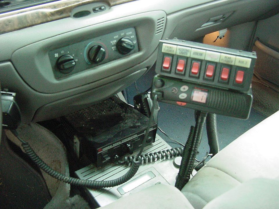 Sedan interior console with HVAC knobs and a bank of red rocker switches plus a two-way radio
