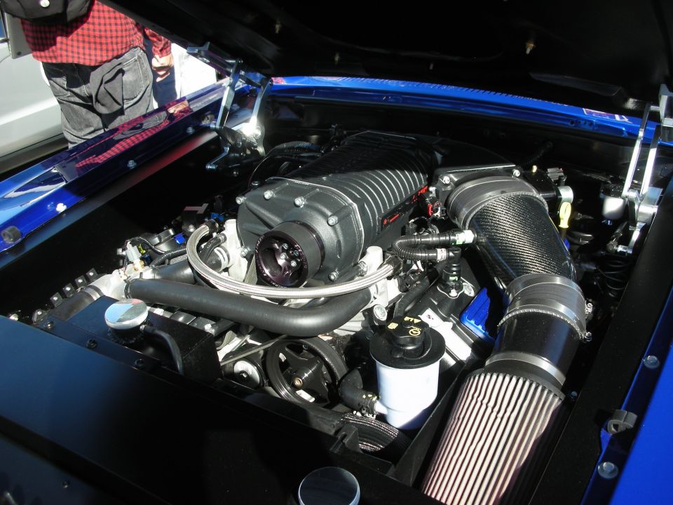 Engine bay with a large black supercharger, carbon fiber intake tube, and air filter