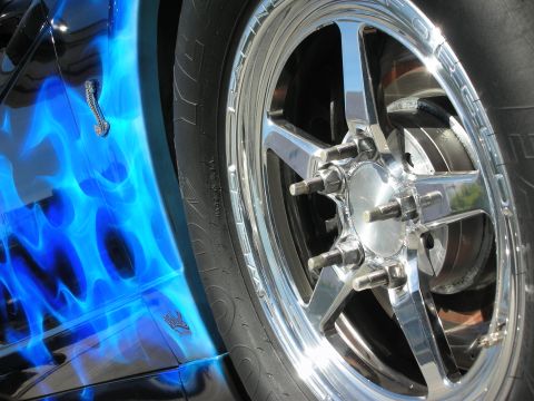 1998 Ford Crown Victoria - A car's side panel features a custom blue flame paint job and a shiny chrome wheel with exposed lug nuts.
