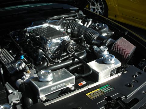 1998 Ford Crown Victoria - Close-up of a modified engine bay, with a yellow Saleen Mustang visible behind it.