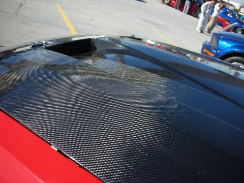 1998 Ford Crown Victoria - A car's hood with a carbon fiber finish and a vent is shown, with other vehicles and people in the background.