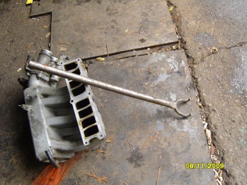 1989 Ford Bronco - An engine intake manifold and a specialized tool are shown on a garage floor.