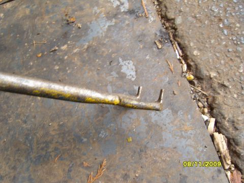 1989 Ford Bronco - A close-up view of a metal tool with yellow paint and two prongs on a dirty surface.