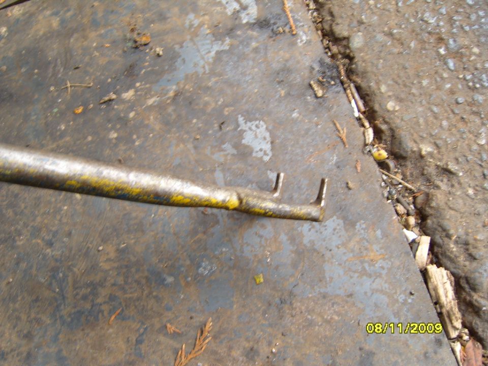 Metal tool with yellow paint and two prongs on a dirty surface