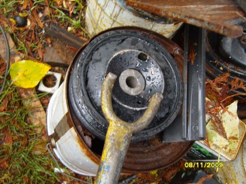 1989 Ford Bronco - A pulley is shown with a yellow tool inserted into its center hole, resting on rusty metal and debris.