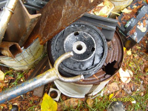 1989 Ford Bronco - Scrap metal and a damaged engine mount sit on a rusty barrel, photographed on 08/11/2009.