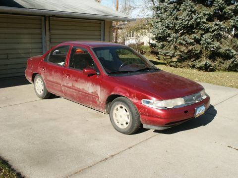 1995 Mercury Mystique - A dusty red sedan sits in a driveway in front of a garage.