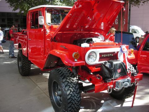 1998 Ford Crown Victoria - A red Toyota Land Cruiser pickup truck is displayed with its hood open, revealing the engine and a winch on the front bumper.