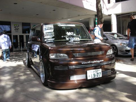 1998 Ford Crown Victoria - A modified brown hatchback is parked in front of a building, with another car visible in the background.
