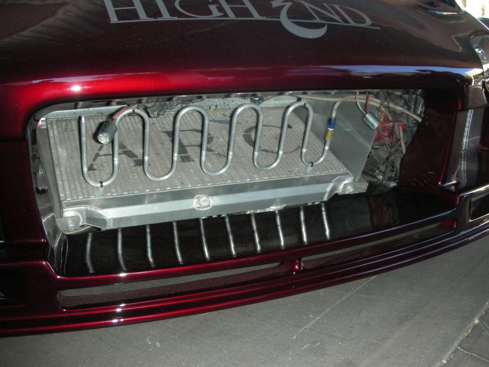 Custom front end of a dark red car showing an exposed, serpentine radiator and a grille with vertical bars. Text on the hood reads 'HIGH END'