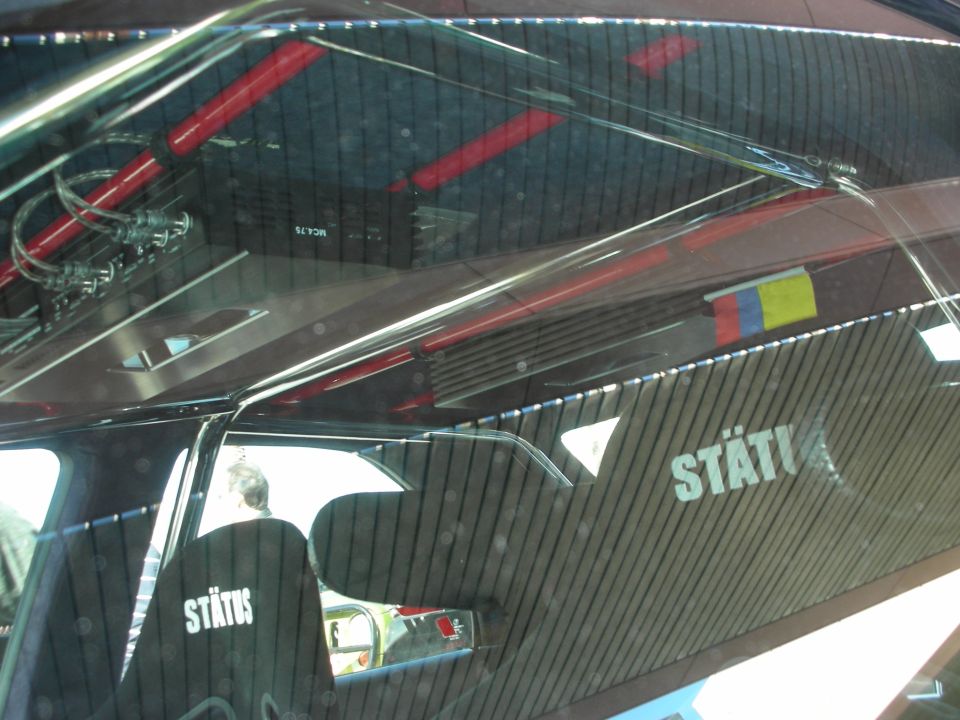 Interior shot of a car with a roll cage, audio amplifier, and seats with 'STATUS' branding