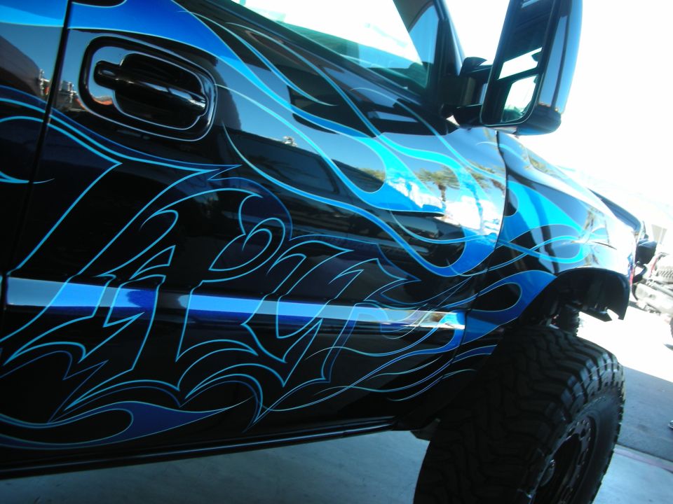 Black truck with custom blue flame graphics, chrome door handle, and large off-road tires