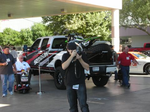1998 Ford Crown Victoria - A Ford Super Duty pickup truck is loaded with a dirt bike and spare tire, with people and other vehicles around.