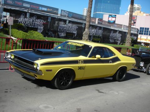 1998 Ford Crown Victoria - Yellow 1970 Dodge Challenger T/A with black stripes and hood scoop is parked outdoors.