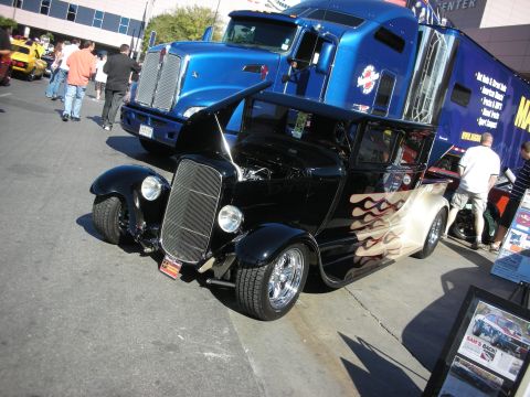 1998 Ford Crown Victoria - A custom black hot rod with flame decals is displayed next to a large blue semi-truck.