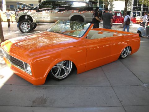 1998 Ford Crown Victoria - An orange convertible pickup truck with custom chrome wheels and a lowered stance is parked on a sidewalk.