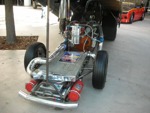1998 Ford Crown Victoria - A custom drag car with its engine exposed is parked next to a red Chevrolet Camaro.