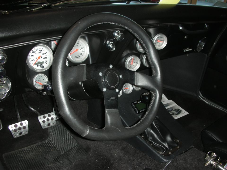 car interior showing steering wheel, dashboard with multiple gauges, and floor pedals