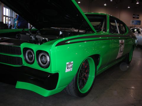 1998 Ford Crown Victoria - A bright green custom car with black racing stripes and custom wheels is displayed indoors with its hood open.