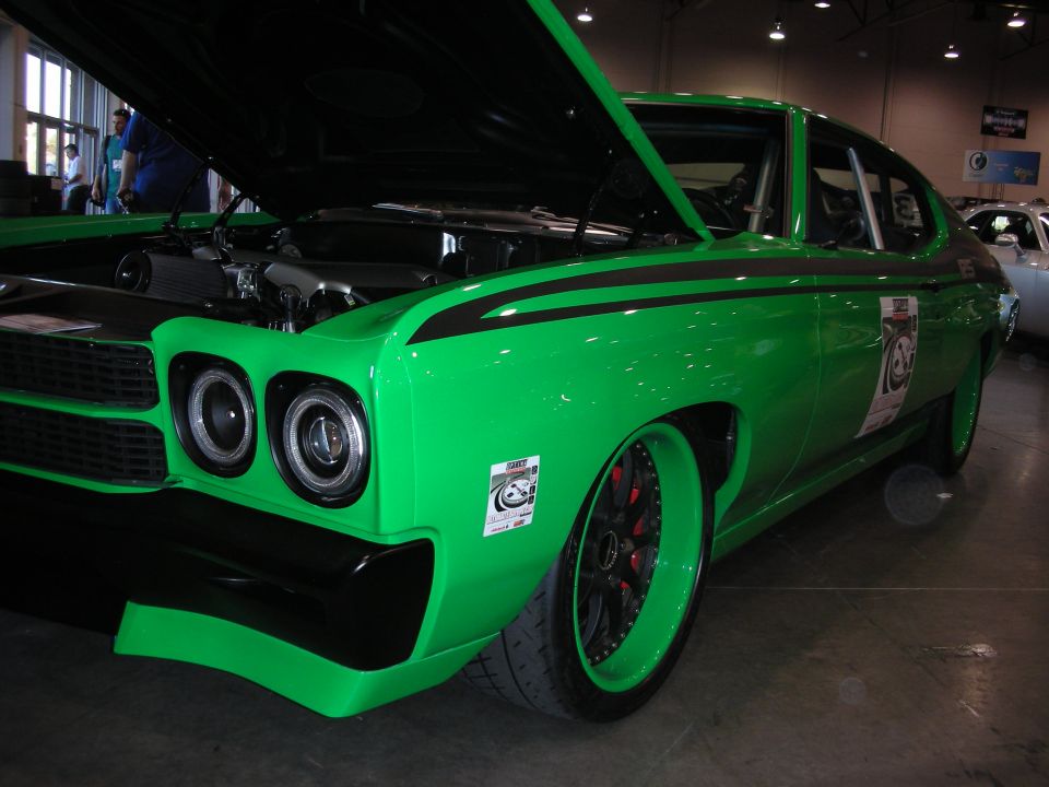 Green muscle car with hood open, showing engine. Black racing stripes on body and hood