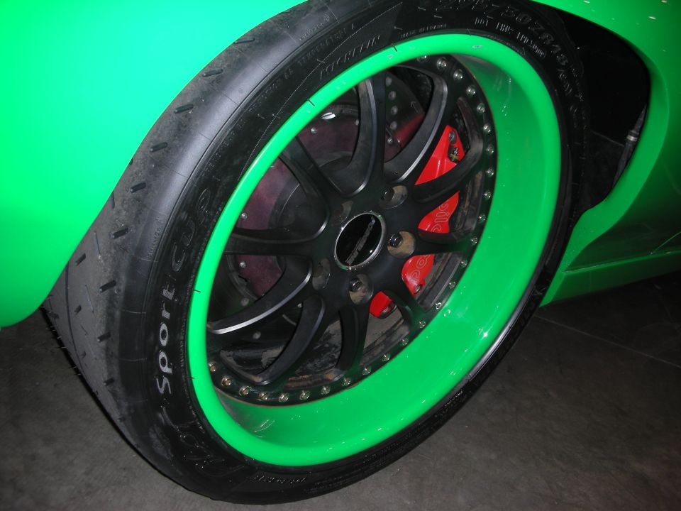 Green car wheel with black spokes, red brake caliper, and bright green rim. Tire has 'Sport Cup' text