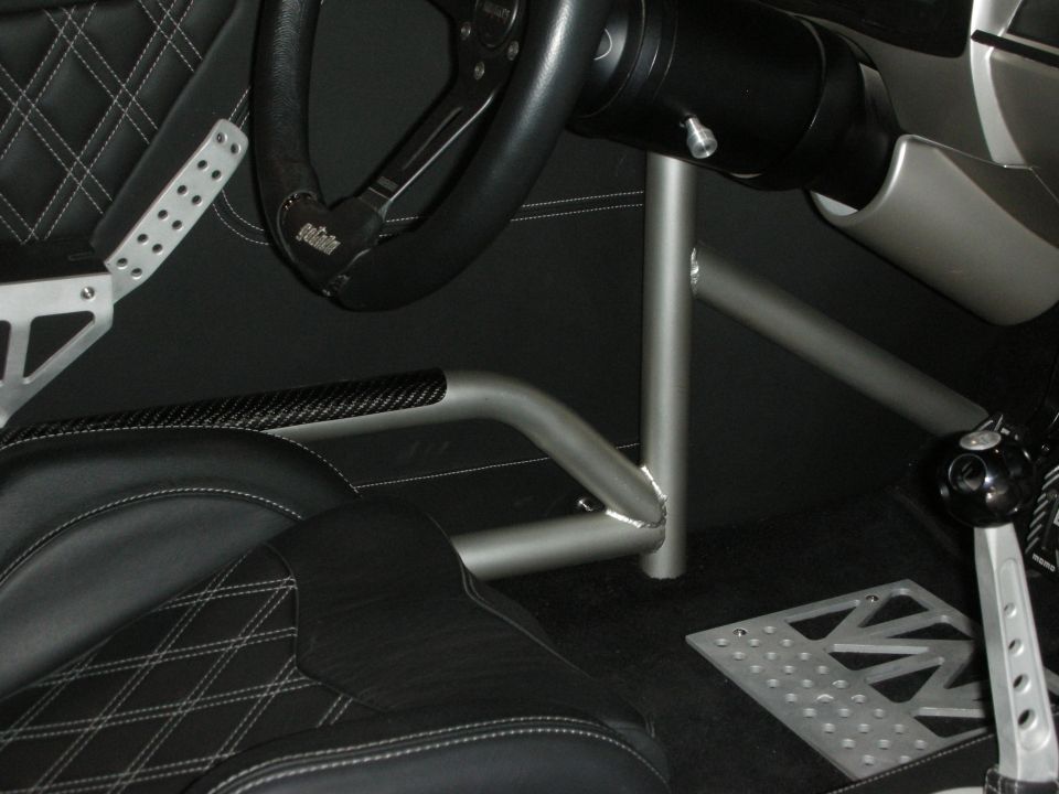 Car interior with black diamond-stitched seats, roll cage, and aftermarket steering wheel