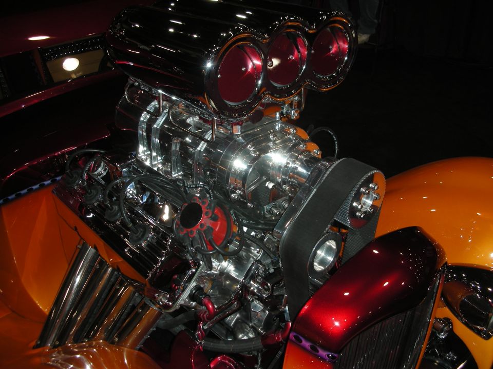 Close-up of a chrome supercharger with three red air intakes on top of a custom engine
