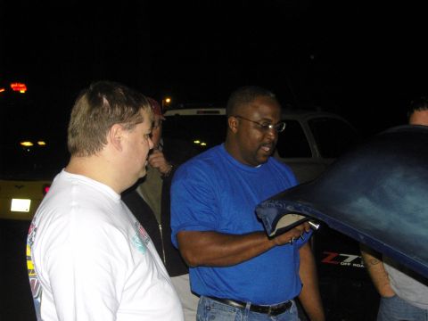 2007 Ford Mustang - People gather around to inspect a car's hood at an outdoor event.