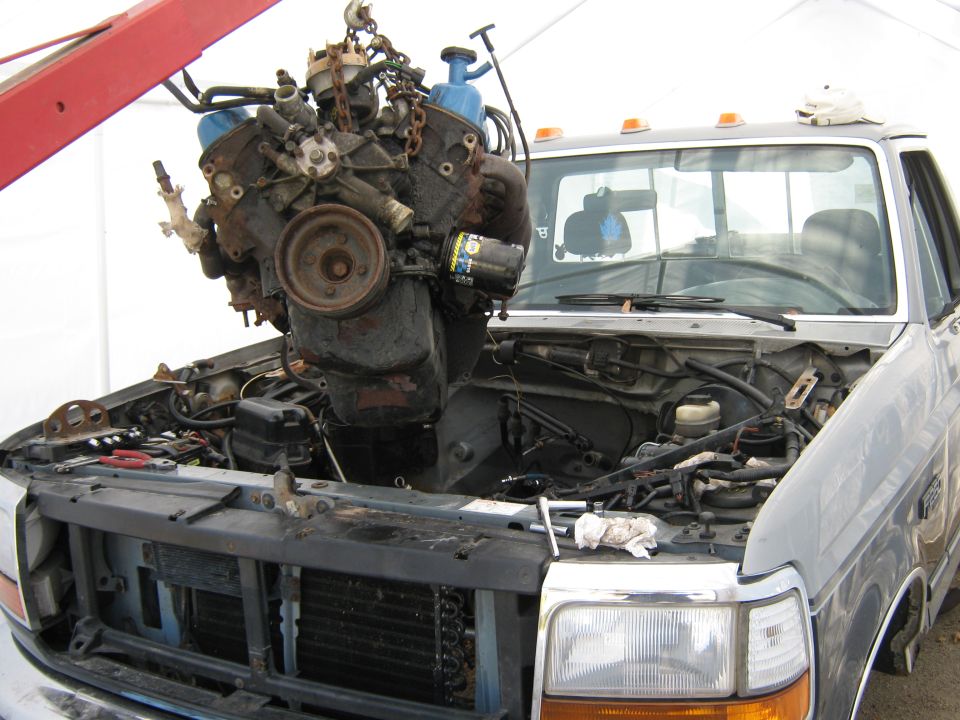 Engine hoist lifting a V8 engine out of a pickup truck with the hood open